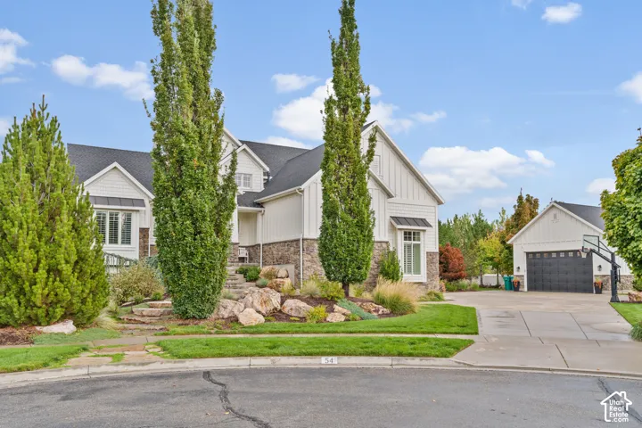 Two-story exterior featuring board-and-batten siding, stone masonry, a detached garage, and tiered landscaping with large boulder accents
