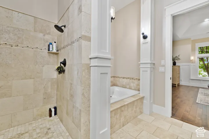 Walk-in shower featuring large-format tile surround, recessed tile shelving, and matte black plumbing fixtures, paired with a built-in soaking tub encased in matching stone tile, defined by architectural column detailing and wall-mounted light fixtures