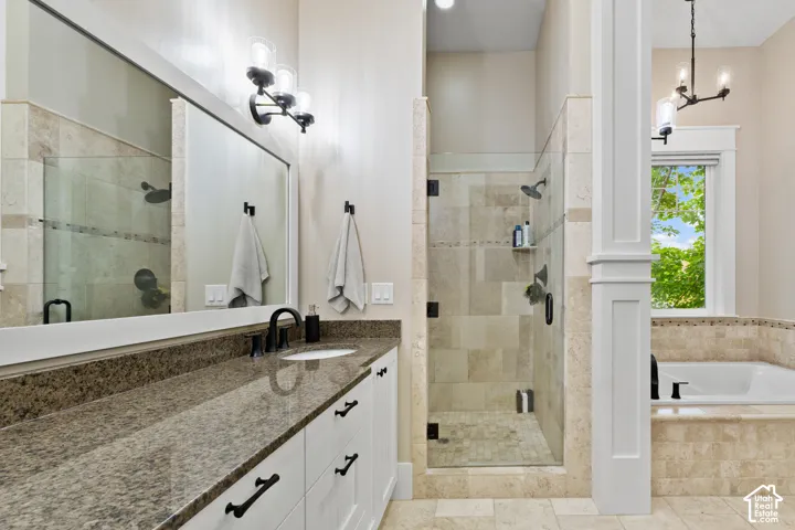 Stone-topped double vanity with undermount sinks, glass-enclosed walk-in shower with stone tile surround, soaking tub with tile surround, and polished metal hardware