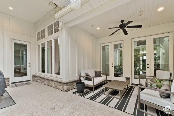 Covered patio featuring board-and-batten siding, stone wainscoting, recessed lighting, a ceiling fan, and three glass-paneled exterior doors