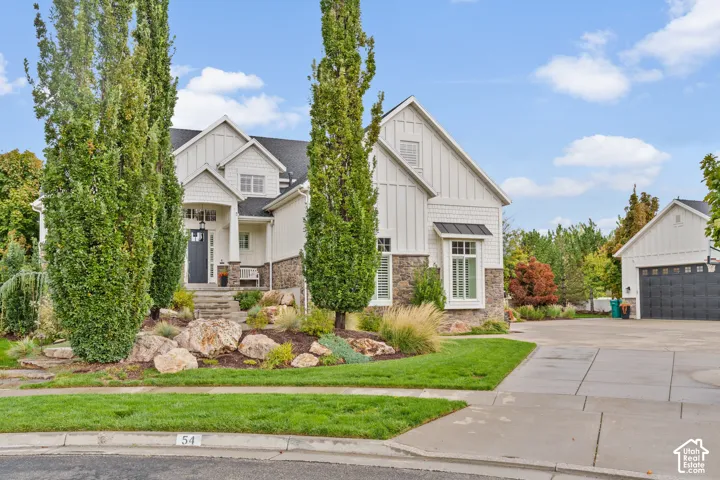 Multi-story residence featuring a board-and-batten exterior, stone masonry veneer, a detached garage, and tiered landscaping with decorative rockery