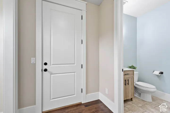 Solid-core door with matte black hardware, wood-finish flooring, wood-tone vanity cabinetry, light-colored tile flooring, and matte black plumbing fixtures