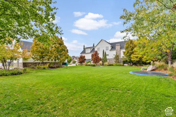 Expansive backyard featuring a manicured lawn, mature trees, stone hardscaping elements, and landscape beds