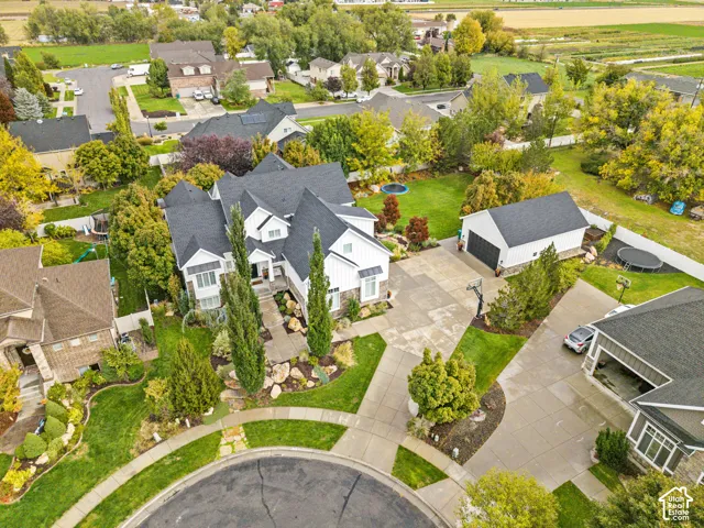 Multi-level residence featuring a high-contrast white and dark shingle exterior, detached garage, extensive concrete driveway, manicured landscaping with stone hardscaping, and a fenced yard