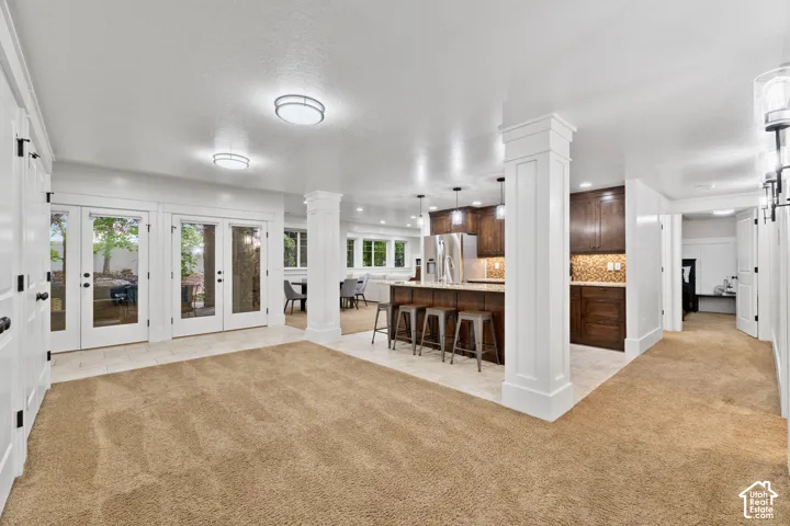 Open-concept interior featuring a kitchen with stained wood cabinetry, stone countertops, a center island, recessed lighting, and double glass doors