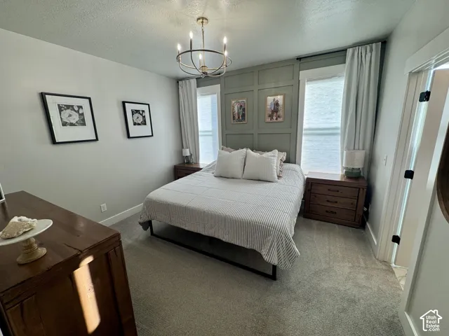 Bedroom featuring a sage green paneled accent wall, neutral carpeting, and a five-arm candelabra-style chandelier