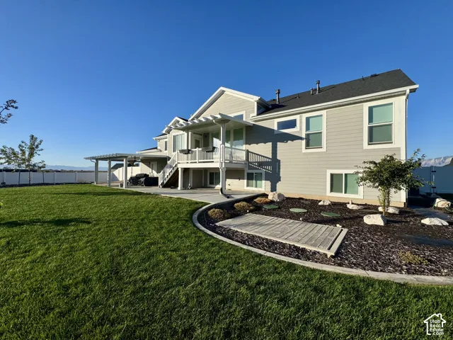 Exterior featuring horizontal siding, a raised deck with a pergola, a concrete patio, and a landscaped yard with stone edging