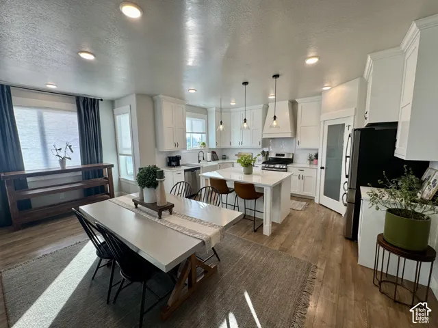Kitchen featuring white cabinetry, center island with stone countertop, stainless steel appliances, pendant lighting, and wood-finish flooring