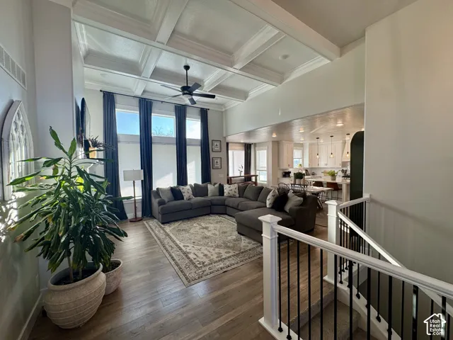 High-ceiling living area featuring coffered ceilings, expansive windows, wood-finish flooring, and a staircase with white balusters and dark metal spindles