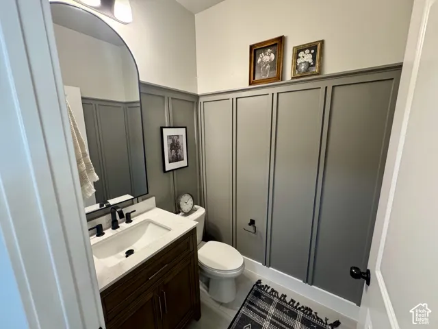 Powder room featuring wall-to-wall board and batten wainscoting, a vanity with a quartz countertop and an integrated rectangular sink, a matte black arched mirror, and coordinating matte black fixtures