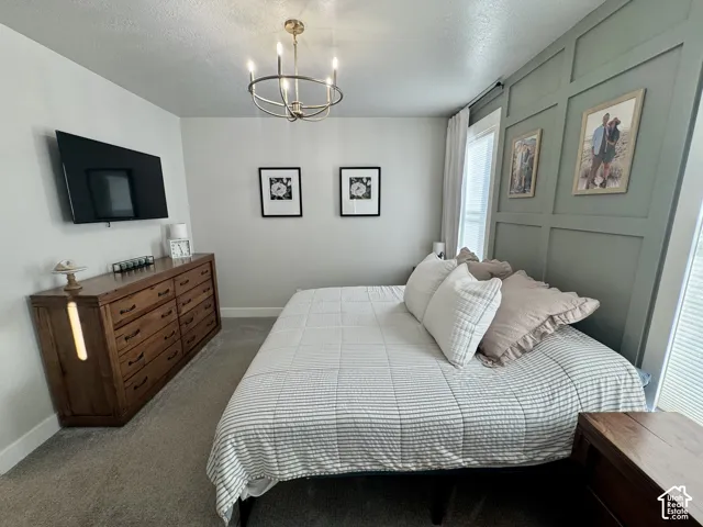 Bedroom featuring a sage green board-and-batten accent wall, neutral carpeting, and a multi-arm metallic chandelier