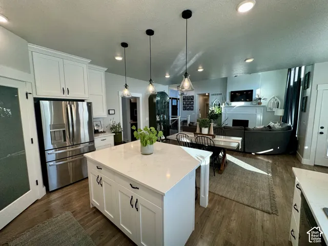 Kitchen featuring a white central island with stone-finish countertops, stainless steel appliances, shaker-style cabinetry, wood-finish flooring, and pendant lighting