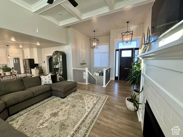 Open-concept interior featuring wood-finish flooring, coffered ceilings, a fireplace with subway tile surround, geometric pendant lighting, and a staircase with a white railing