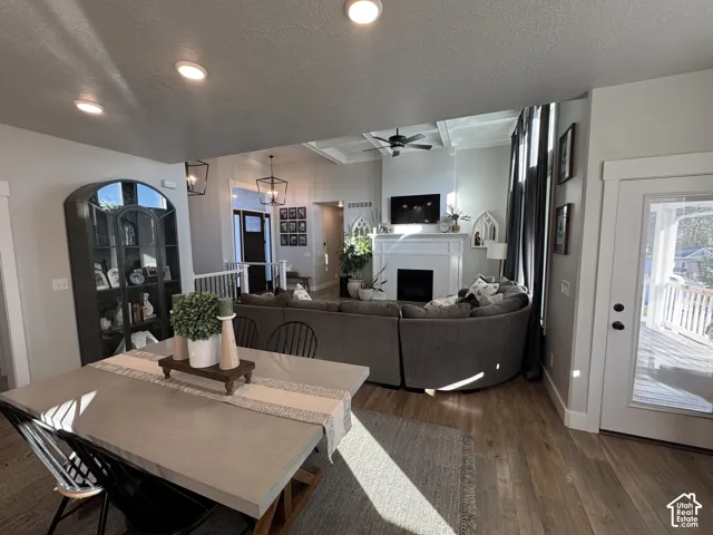 Open-concept interior featuring wood-finish flooring, a coffered ceiling with a center fan, a fireplace with a white mantel, built-in shelving, and recessed lighting