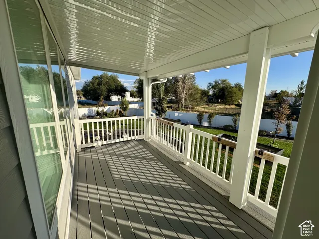Covered deck featuring composite decking, white vertical railings, a beadboard ceiling, and full-length windows