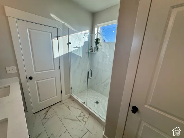 Walk-in glass-enclosed shower featuring large-format tile surround, integrated shower shelving, white hexagonal floor tiling, and a crisp white vanity with a solid-surface countertop