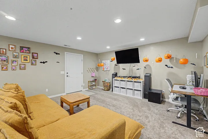 Recessed ceiling lighting illuminates a spacious room featuring neutral wall tones and textured carpeting