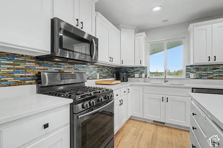 White cabinetry with black hardware, stainless steel appliances, a multi-tone tile backsplash, and light wood-finish flooring