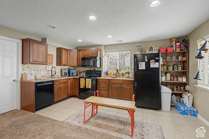 Wood-finish cabinetry, black appliances, tile flooring, and recessed lighting