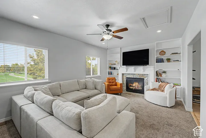Living area featuring a stone surround fireplace with white mantel, built-in shelving, a ceiling fan, and recessed lighting