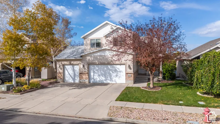 Two-story property featuring a multi-tone exterior, two garage doors, a concrete driveway, and established landscaping