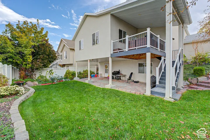 Expansive backyard with a manicured lawn, a raised deck with white railings, and a lower-level patio