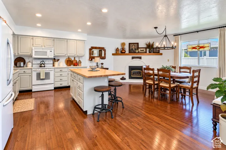 Kitchen featuring wood-finish flooring, cabinetry with white finish, a central island with a wood countertop, recessed ceiling lighting, and a painted brick fireplace