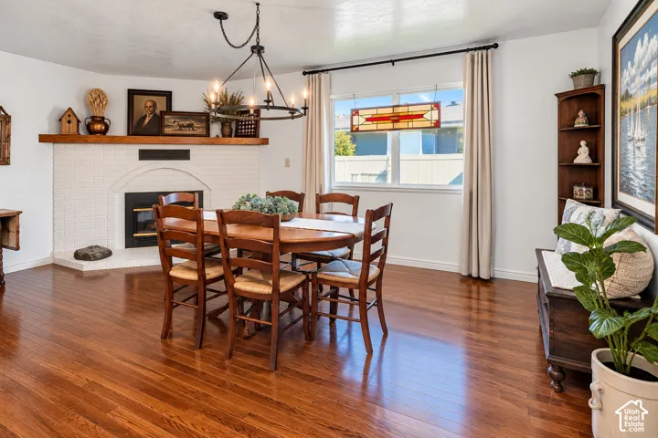 White painted brick fireplace featuring a wood mantel, wood-finish flooring, custom iron chandelier, and a decorative stained-glass window insert