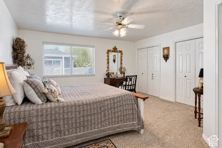 Neutral carpeted flooring, two sets of white six-panel closet doors, and a ceiling-mounted light fixture with a central fan