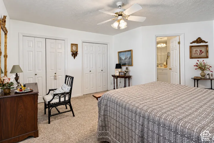 Bedroom featuring neutral carpeting, two sets of bifold closet doors, and a central ceiling fan with integrated lighting
