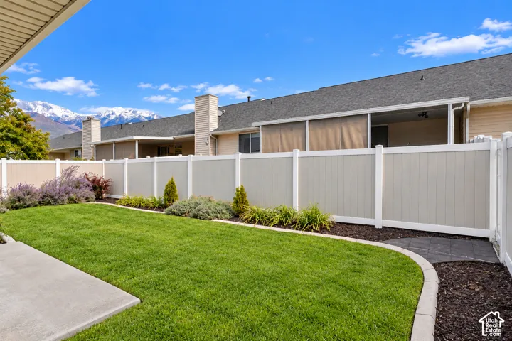 Private backyard featuring a manicured lawn, concrete patio, perimeter vinyl fencing, and mountain backdrop