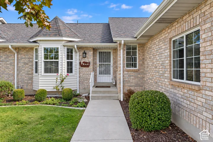 Exterior facade featuring brick masonry, a multi-faceted bay window, shingle roofing, and a concrete entryway path