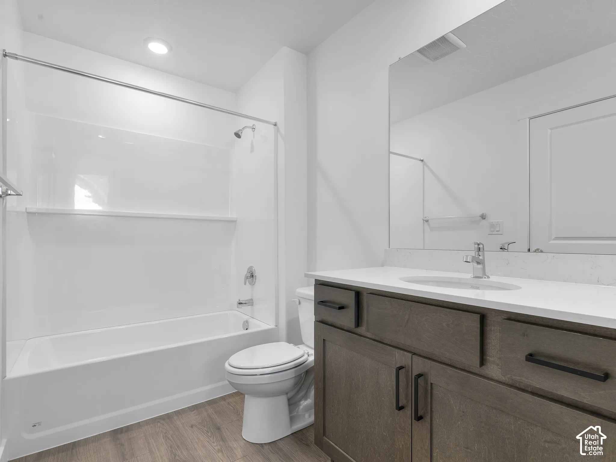 Bathroom featuring a dark wood-finish vanity with a light-toned countertop, integrated oval sink, matte black hardware, and a tub-shower combination with a full-width mirror