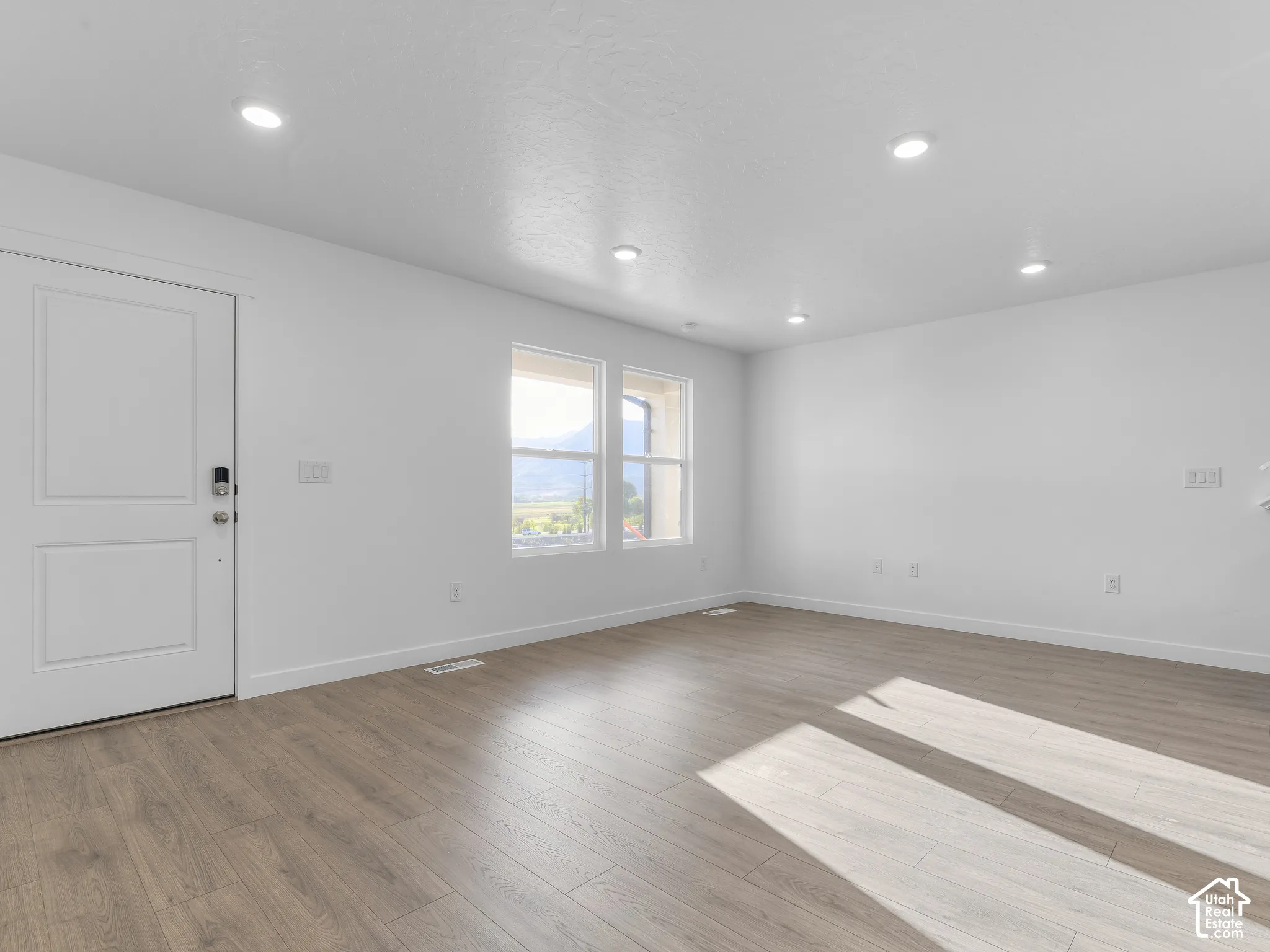 Interior space featuring wood-finish flooring, recessed lighting, dual windows, and a paneled entry door
