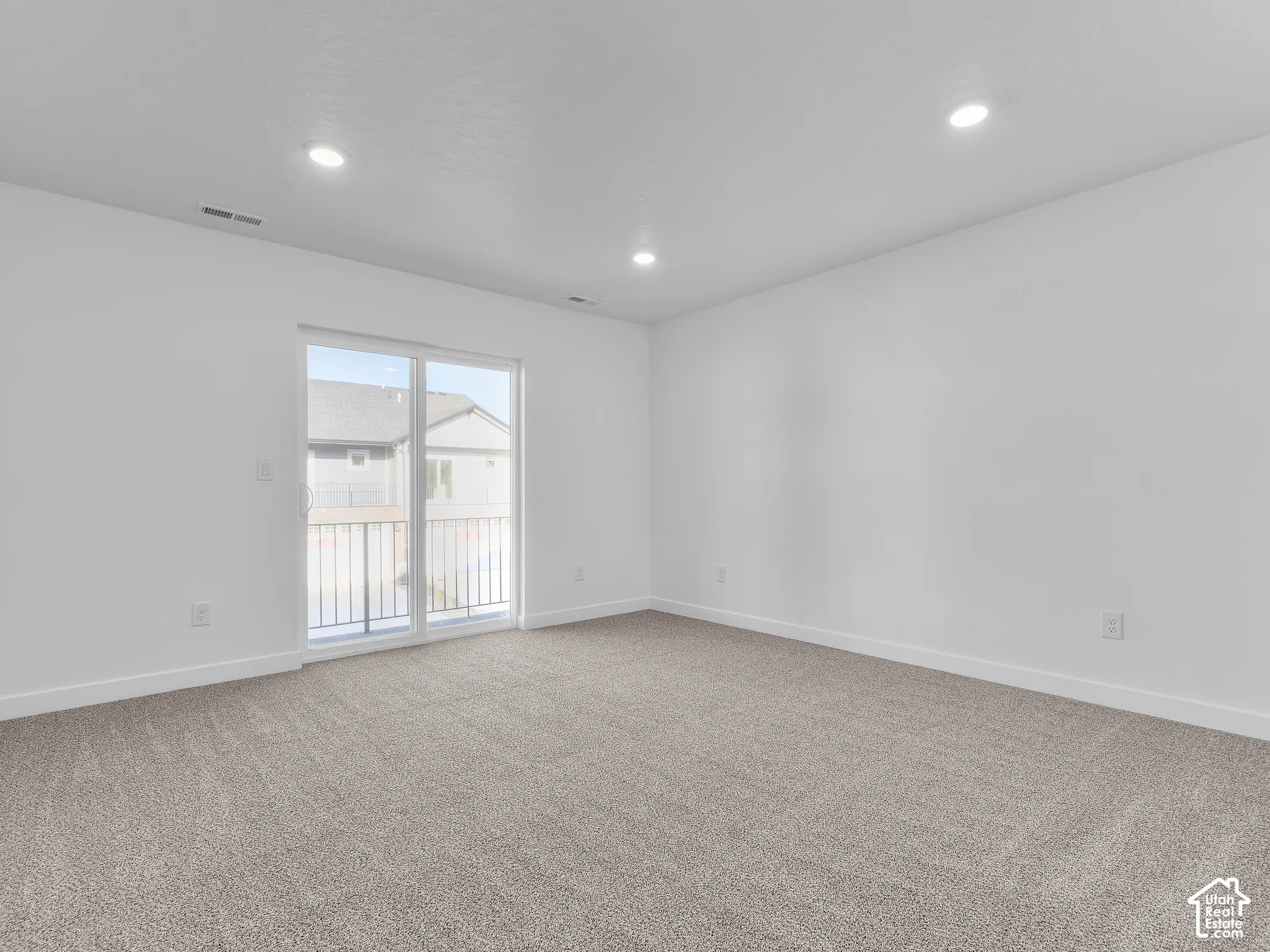 Neutral-toned wall-to-wall carpeting, recessed ceiling lighting, and sliding glass door with access to a railed exterior space