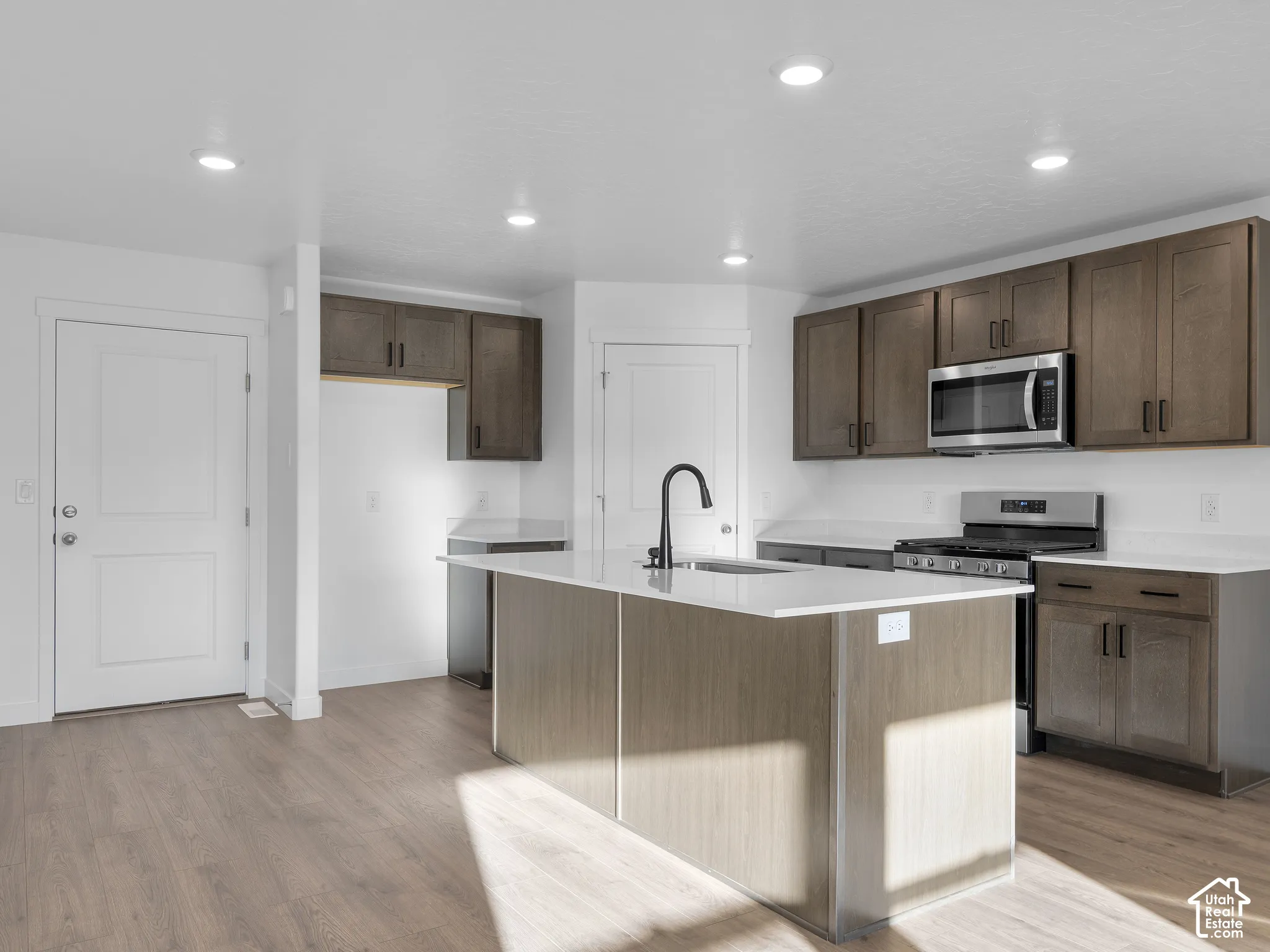 Kitchen featuring a center island with a stone-surface countertop, dark-finish cabinetry, recessed lighting, stainless steel appliances, and wood-finish flooring