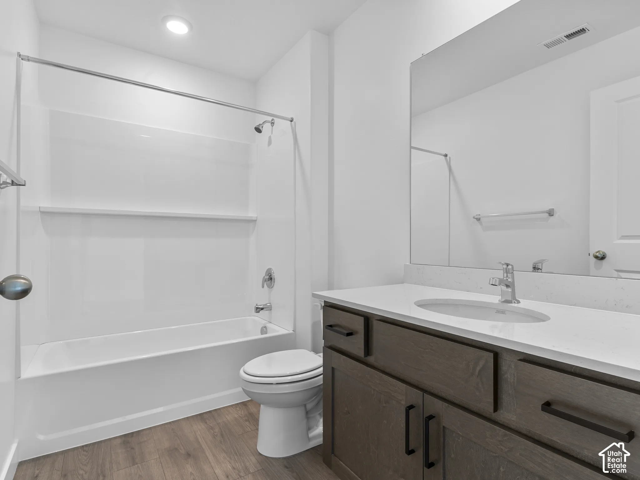 Bathroom featuring a vanity with wood-finish cabinetry, quartz countertop, an integrated oval sink, and a combination tub and shower surround with wood-finish flooring