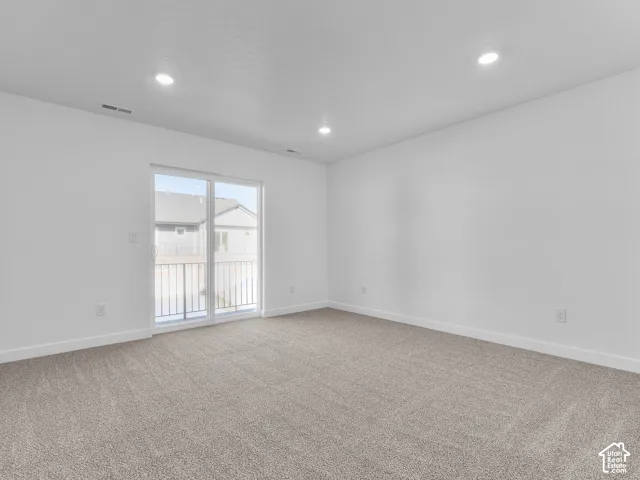 Neutral-toned wall-to-wall carpeting, recessed ceiling lighting, and sliding glass door with access to a railed exterior space