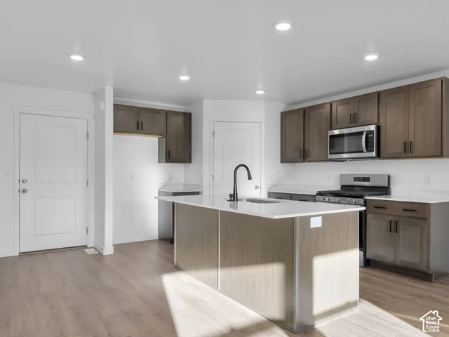 Kitchen featuring a center island with a stone-surface countertop, dark-finish cabinetry, recessed lighting, stainless steel appliances, and wood-finish flooring