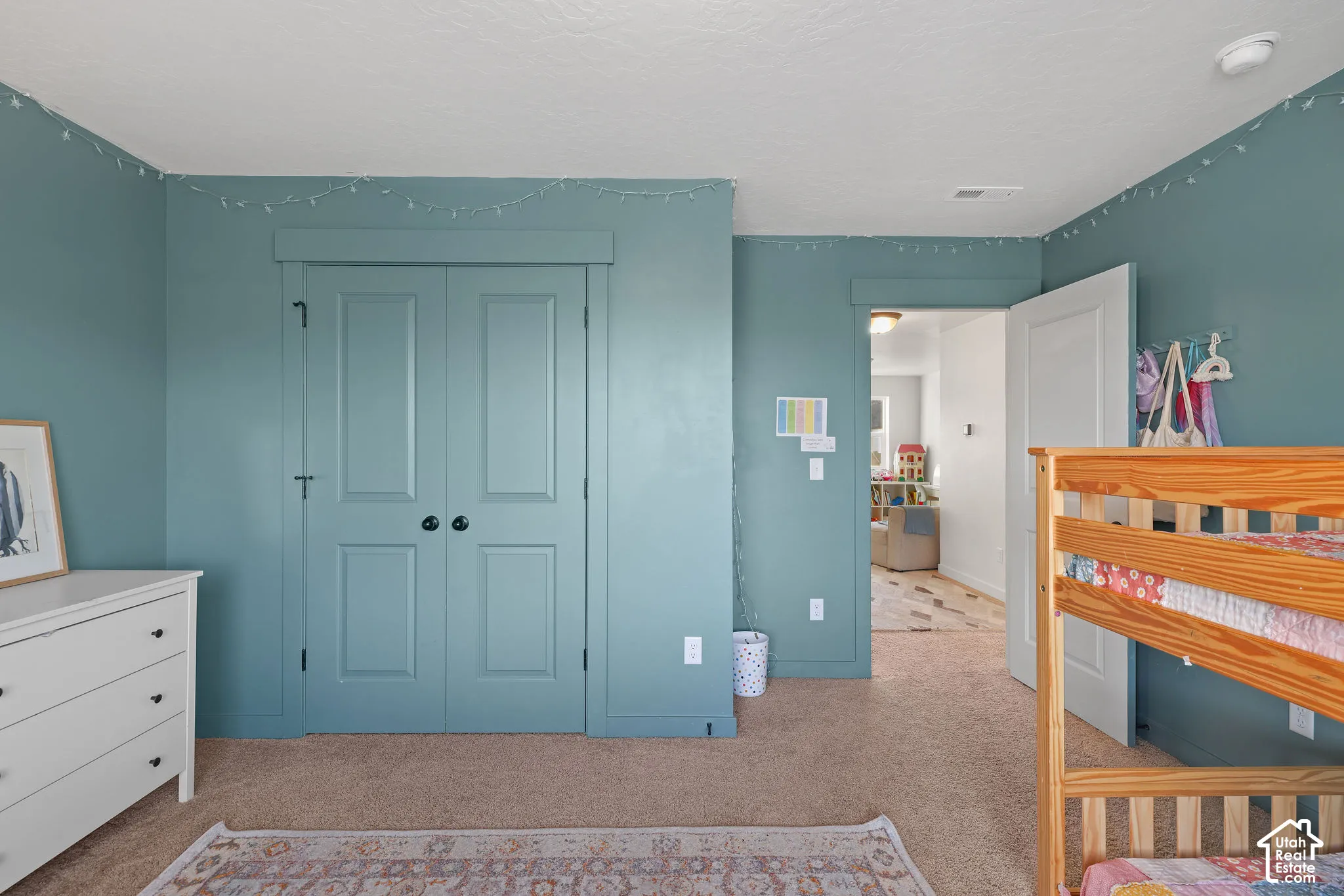 Interior space featuring teal-toned wall paint, neutral carpeting, and a double-door closet with custom door casing