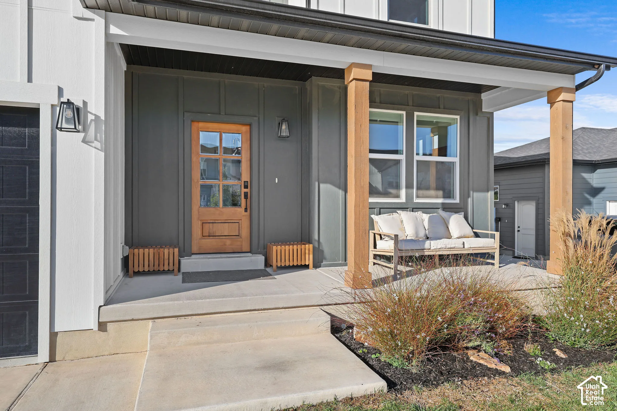 Covered front porch featuring board-and-batten siding, natural wood support columns, and a six-panel wood entry door with glass inserts