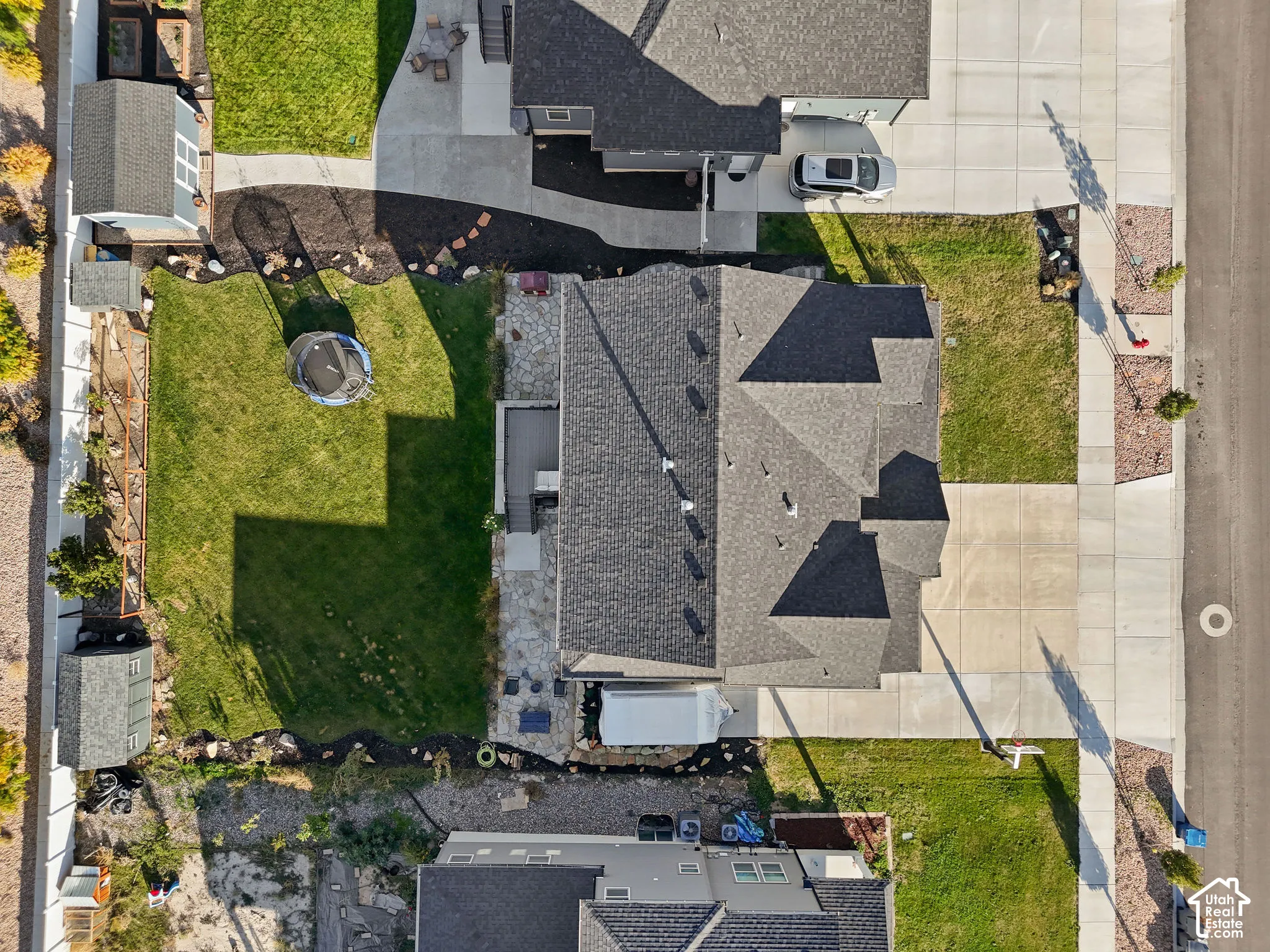 Aerial perspective of property featuring a multi-pitched asphalt shingle roof, concrete driveway, stone patio, fenced perimeter, and dedicated storage structure