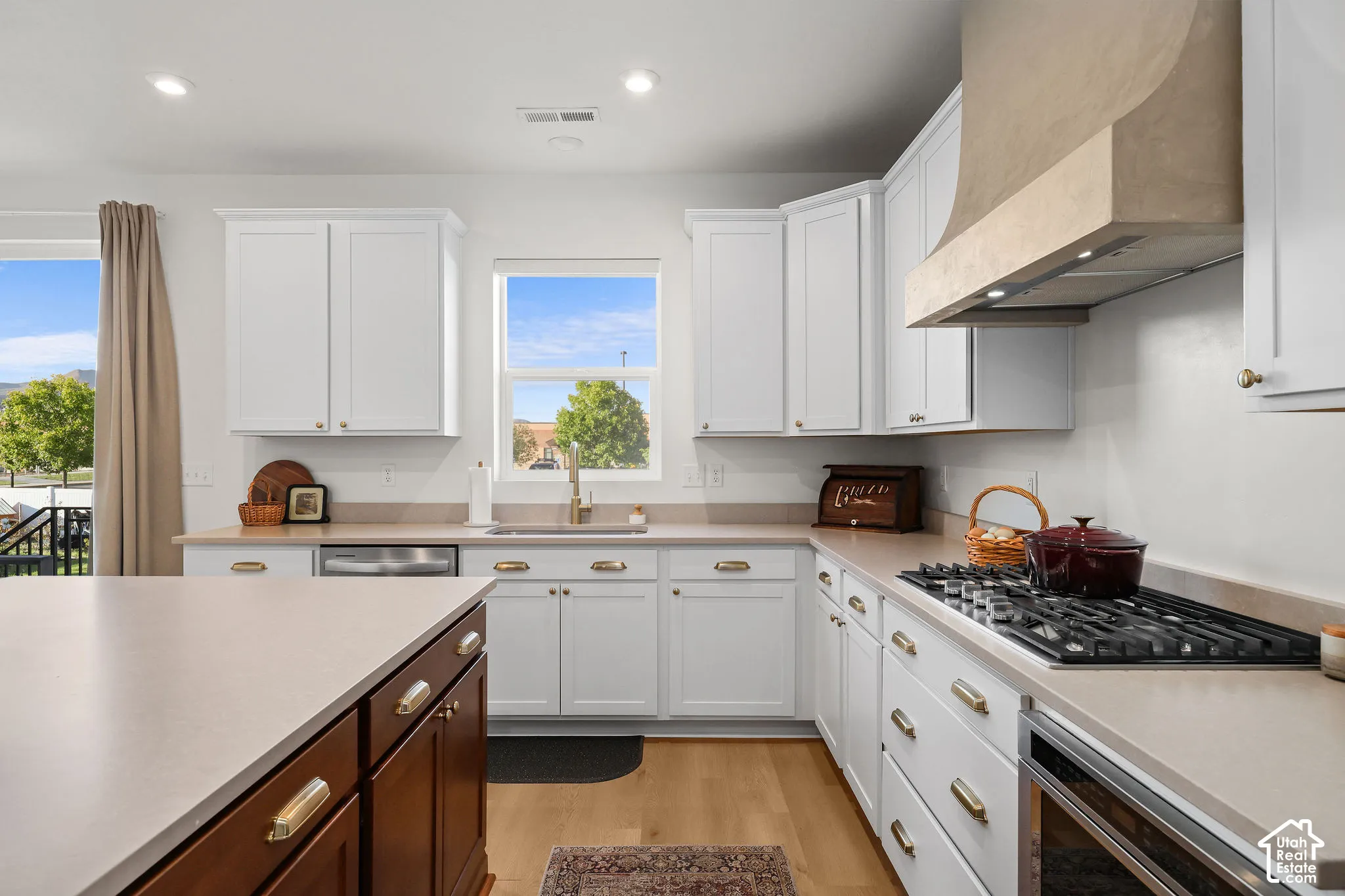 Kitchen featuring white shaker-style cabinetry, a contrasting wood-finish kitchen island, a custom range hood, recessed lighting, and wood-finish flooring