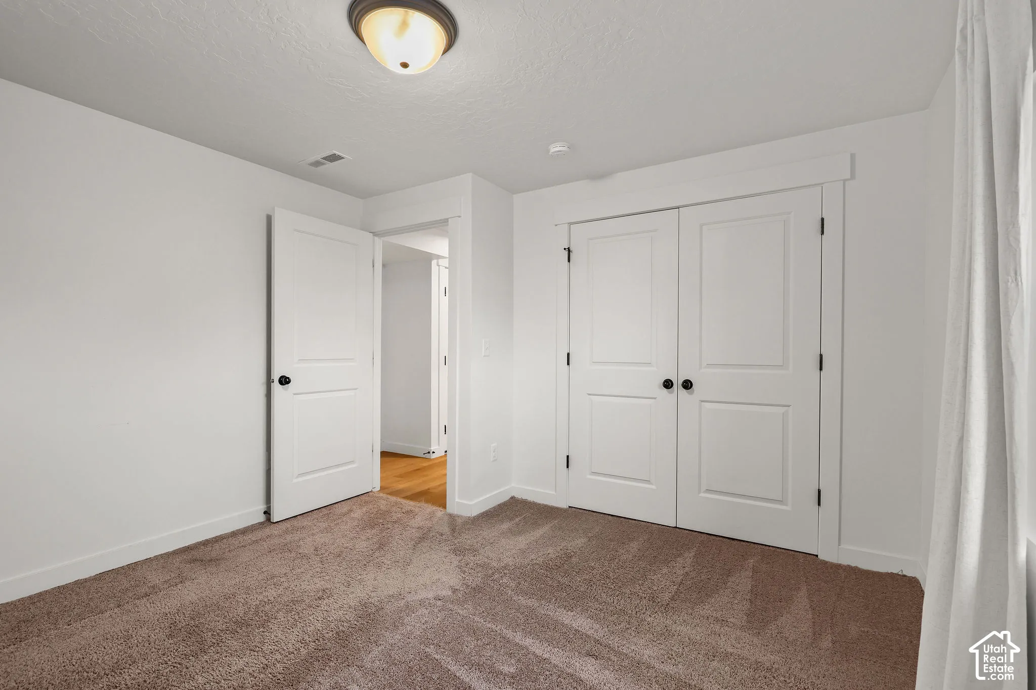 Neutral interior featuring wall-to-wall carpeting, two-panel interior doors, double-door closet with trim casing, and a flush-mount ceiling light fixture