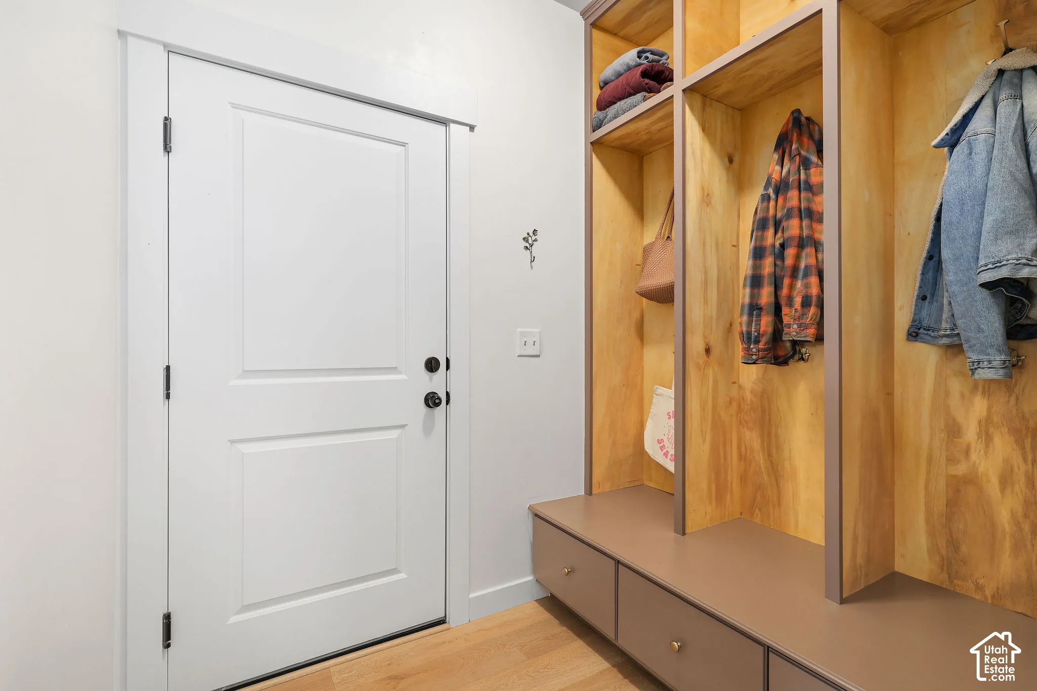 Custom built-in wood cabinetry featuring upper storage cubbies, integrated coat hooks, and lower bench seating with three pull-out drawers, complemented by wood-finish flooring and a solid core entry door
