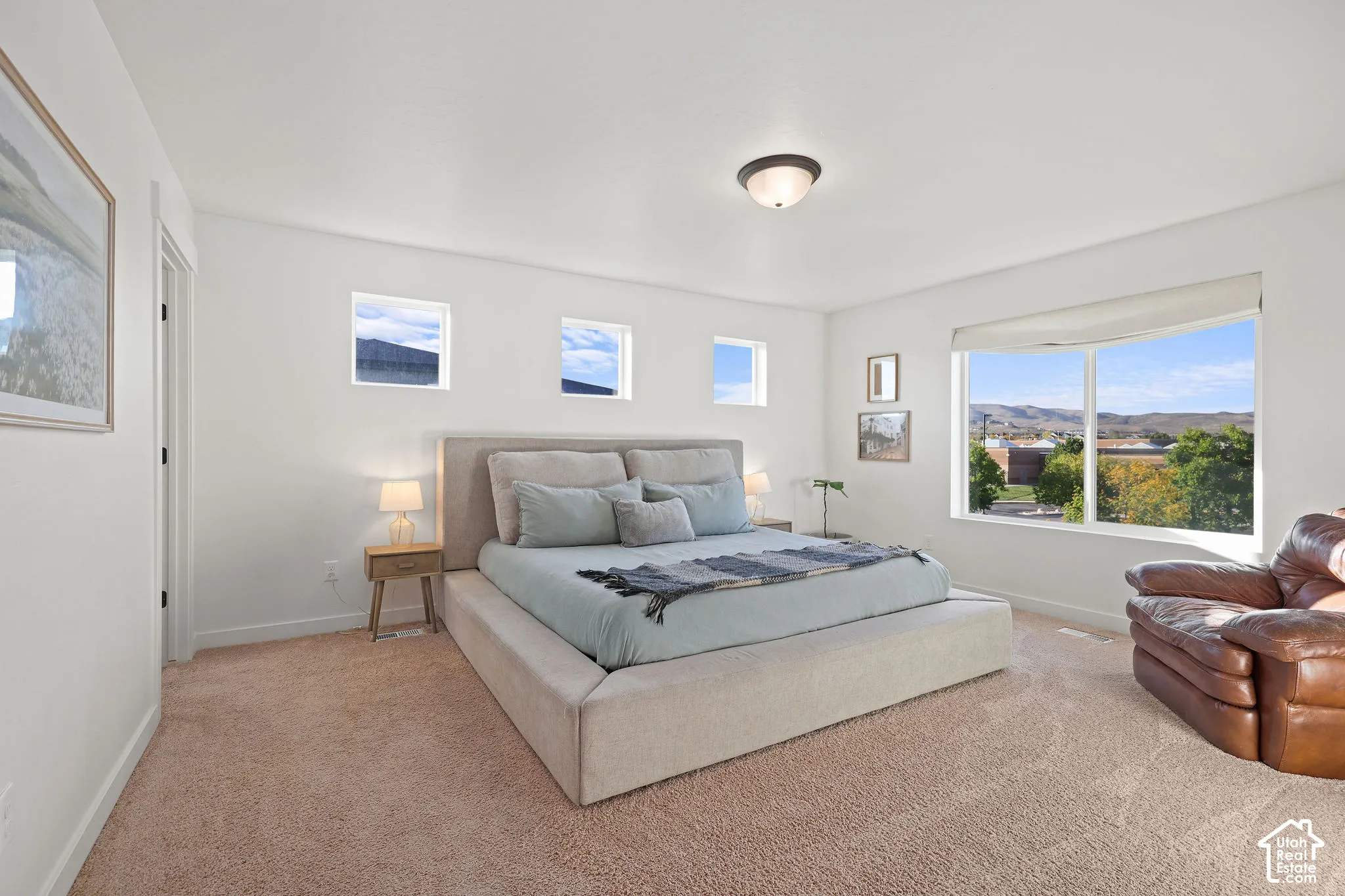 Neutral-toned bedroom featuring carpeting, large picture windows, three square upper-wall windows, and a ceiling-mounted light fixture