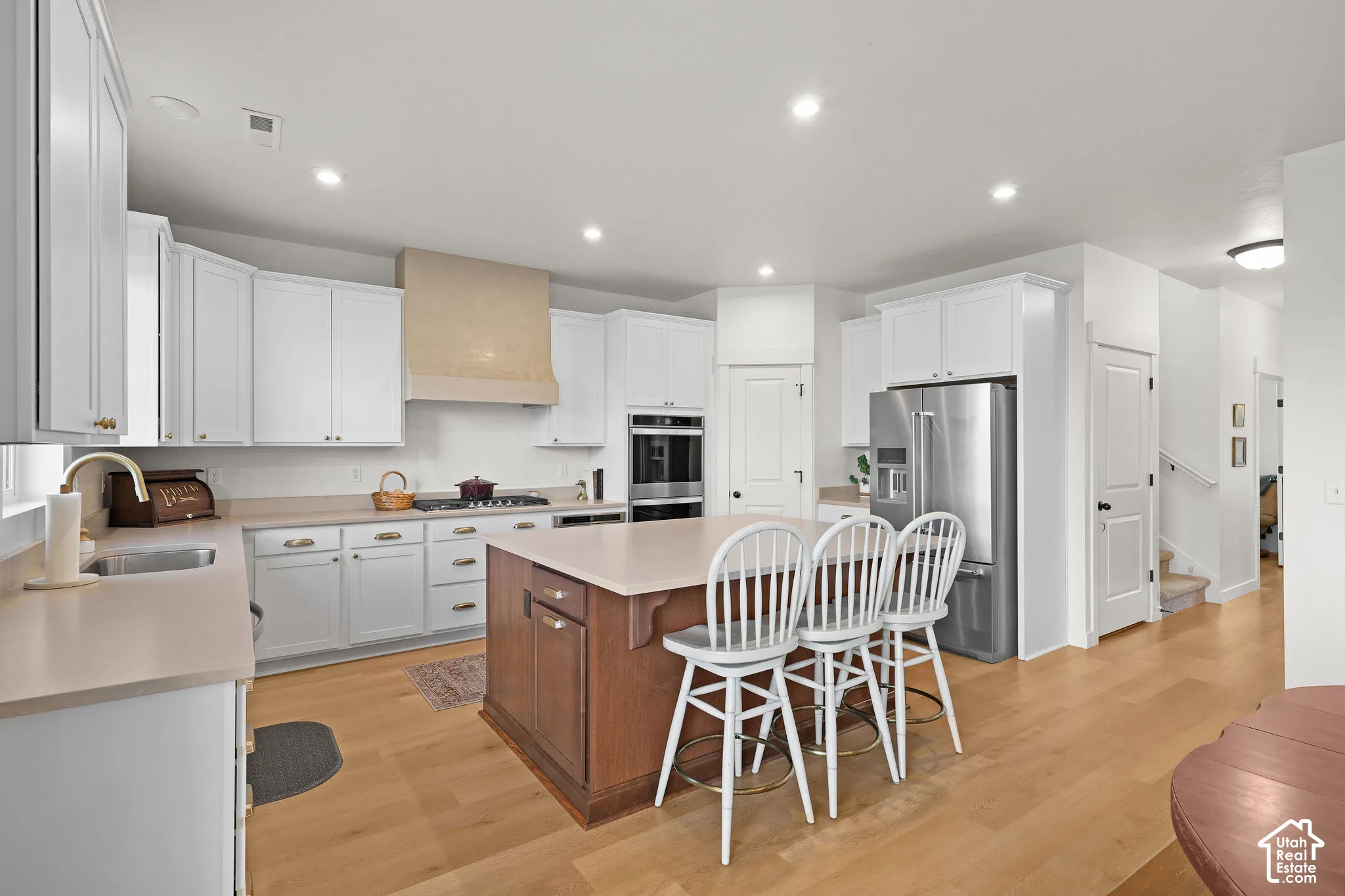 Kitchen featuring a central island with wood-finish cabinetry, solid-surface countertops, stainless steel wall-mounted oven, custom-built vent hood, and recessed lighting