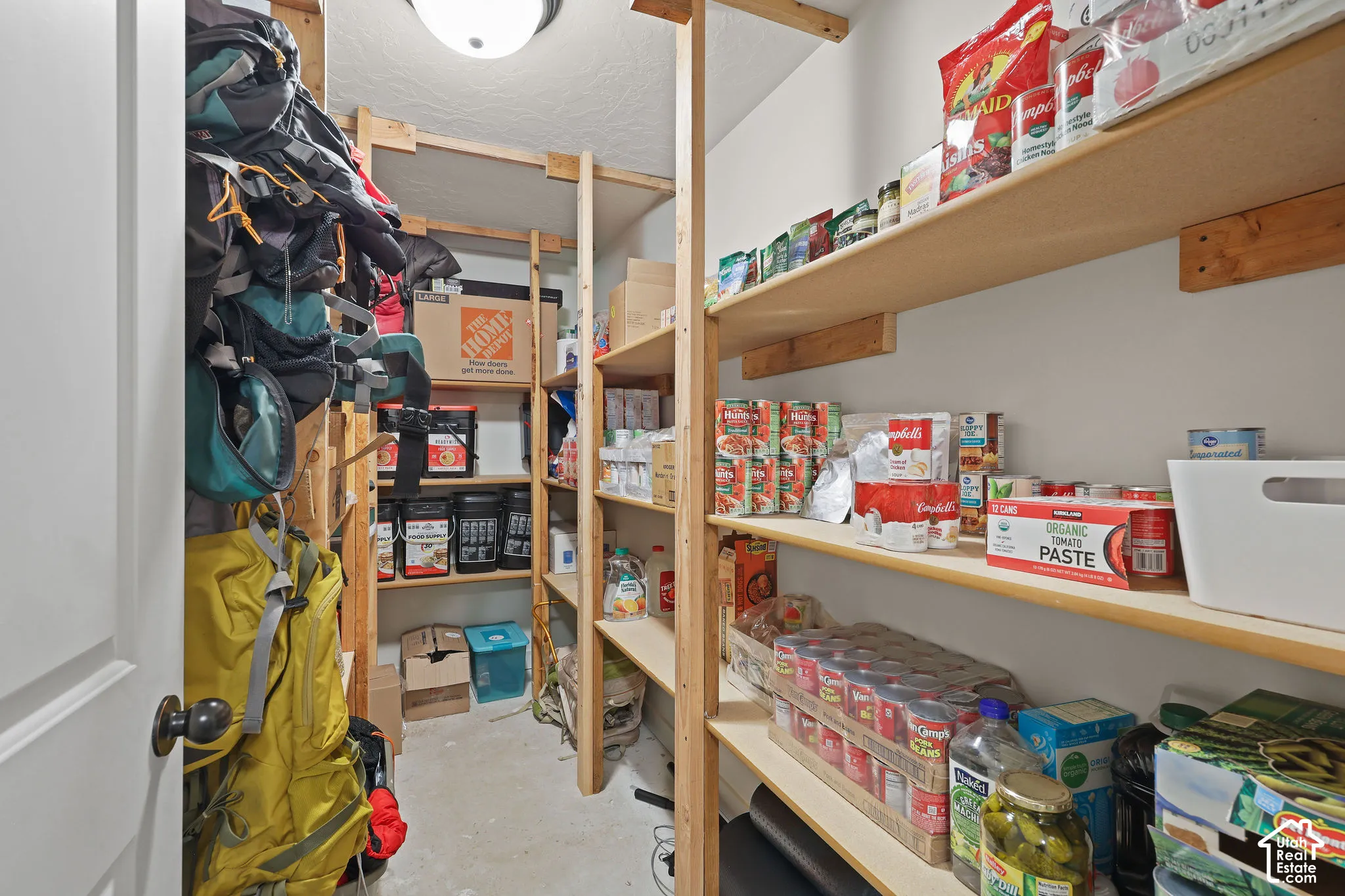 Walk-in storage pantry featuring multiple tiers of open wooden shelving and a ceiling-mounted light fixture