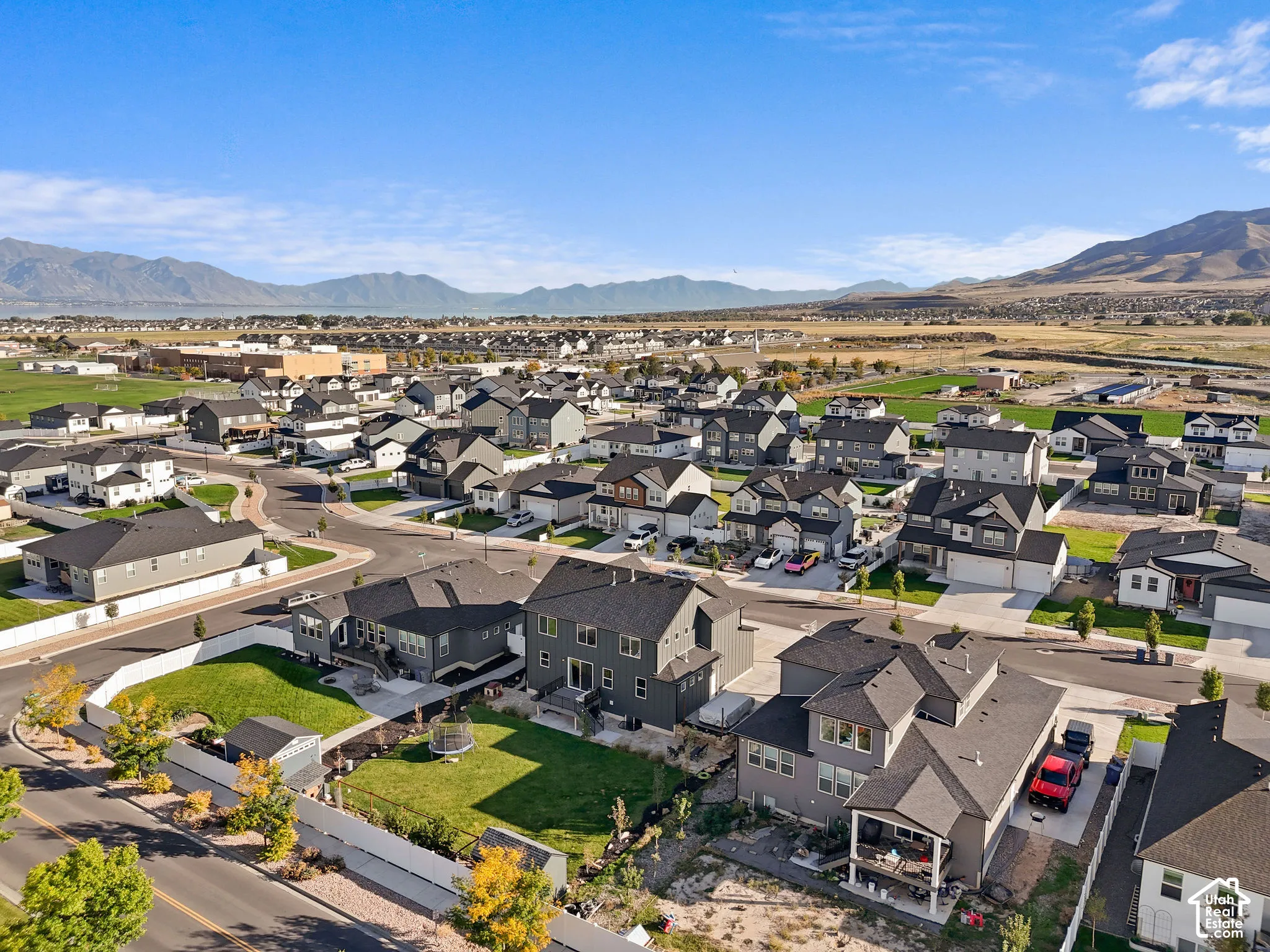 Aerial perspective featuring multi-story residential structures, fenced rear yards with manicured lawns, asphalt roadways, and mountainous topography