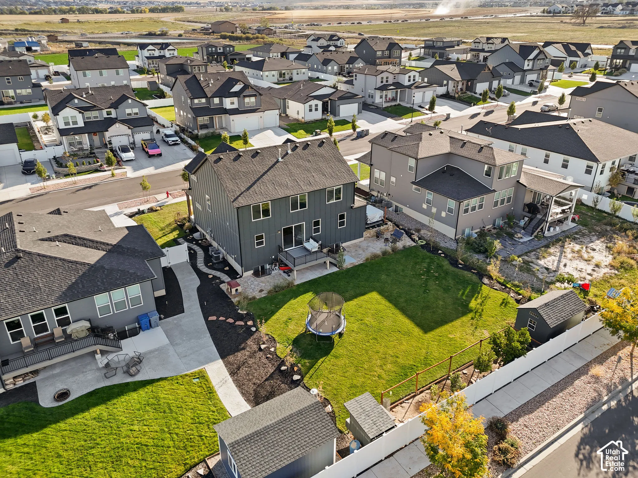 Two-story residence with vertical siding, elevated rear deck, fenced backyard, manicured lawn, and detached storage structure